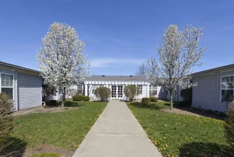 Pathway to Cardinal Place entrance, a single-story senior living building with blooming trees.