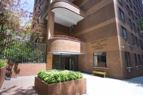 Exterior view of Cumberland Gardens entrance with brick facade, planter, and bench.