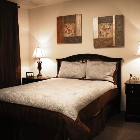 Cozy bedroom with a made bed, two bedside tables and lamps, and framed artwork above the headboard.