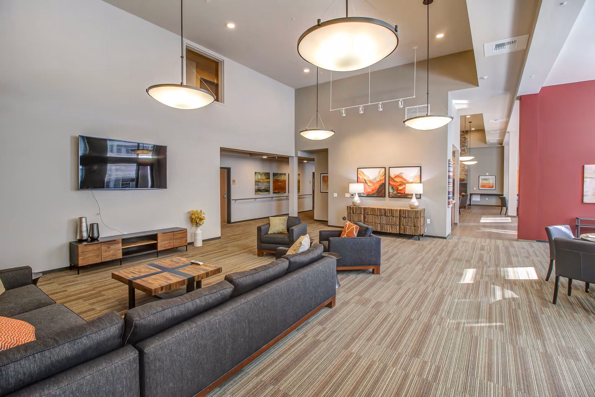 Spacious modern common lounge with sofas, armchairs, a wall-mounted TV, pendant lights, and artwork.