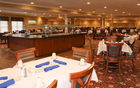 Senior living dining room with round tables, white tablecloths, and a long serving counter.