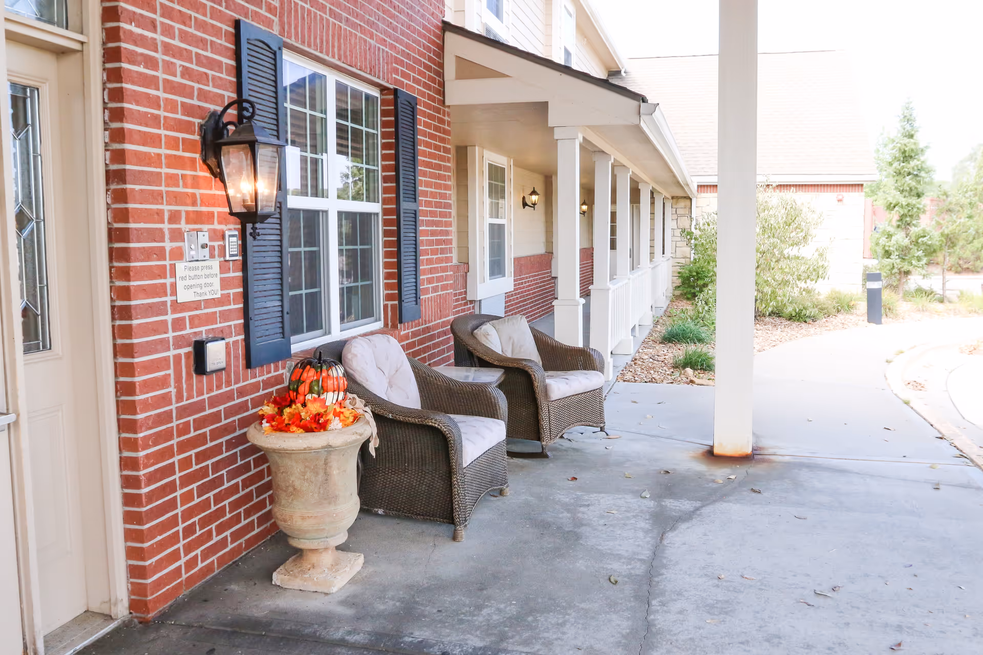 Covered brick entrance porch with wicker chairs, a decorative planter, and a walkway.
