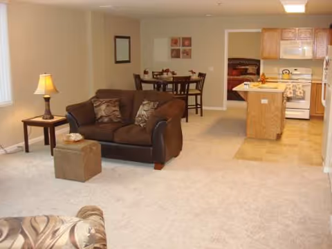 Living area with sofa, lamp, dining table, open kitchen, and a view into a bedroom.