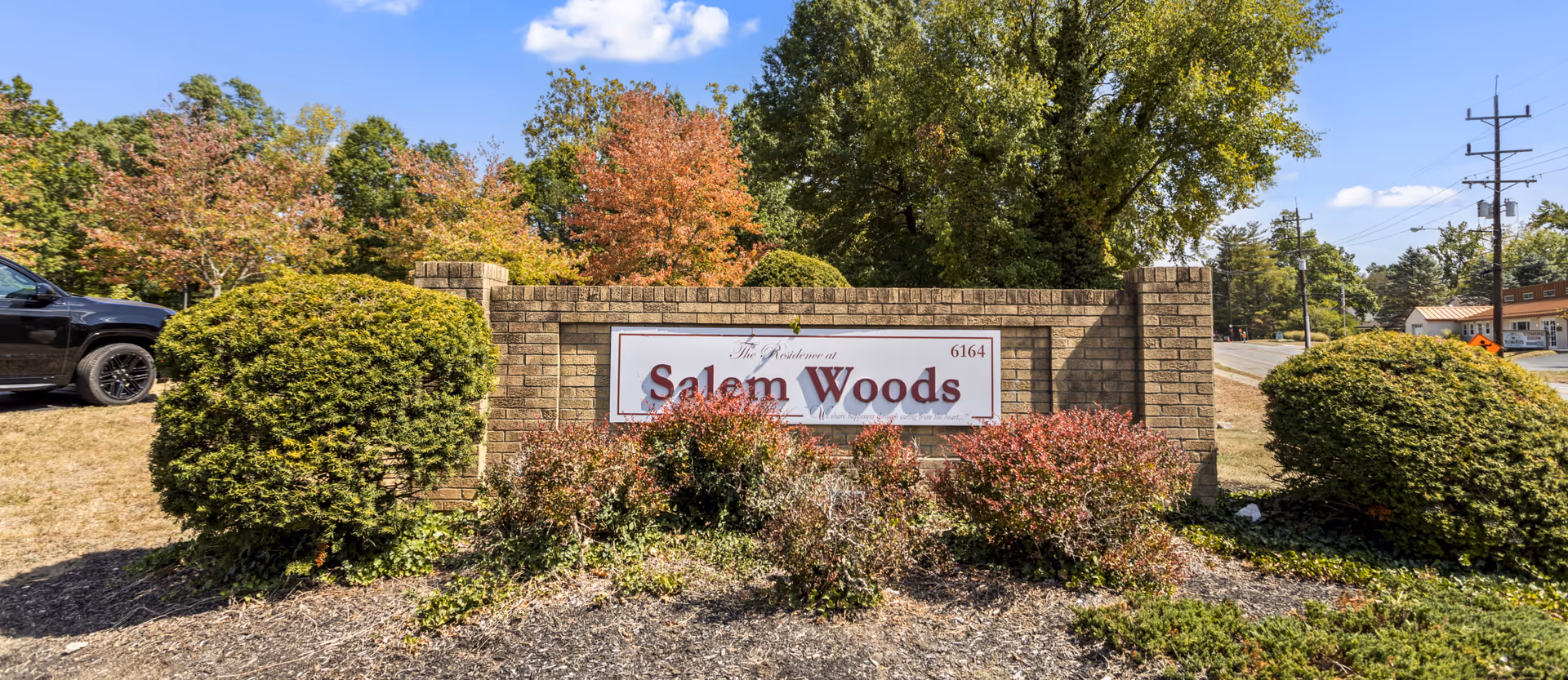 Brick sign at the entrance of Residence at Salem Woods surrounded by bushes and trees with a clear blue sky in the background.