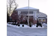 Exterior view of the RiverWoods Senior Living Community building entrance during winter, with snow on the ground and leafless trees surrounding the driveway.