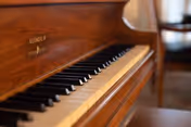 Close-up view of a wooden piano keyboard with black and white keys, with a blurred chair and table in the background.