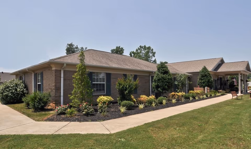 Single-story brick senior living facility with a landscaped front, walkway, and benches.