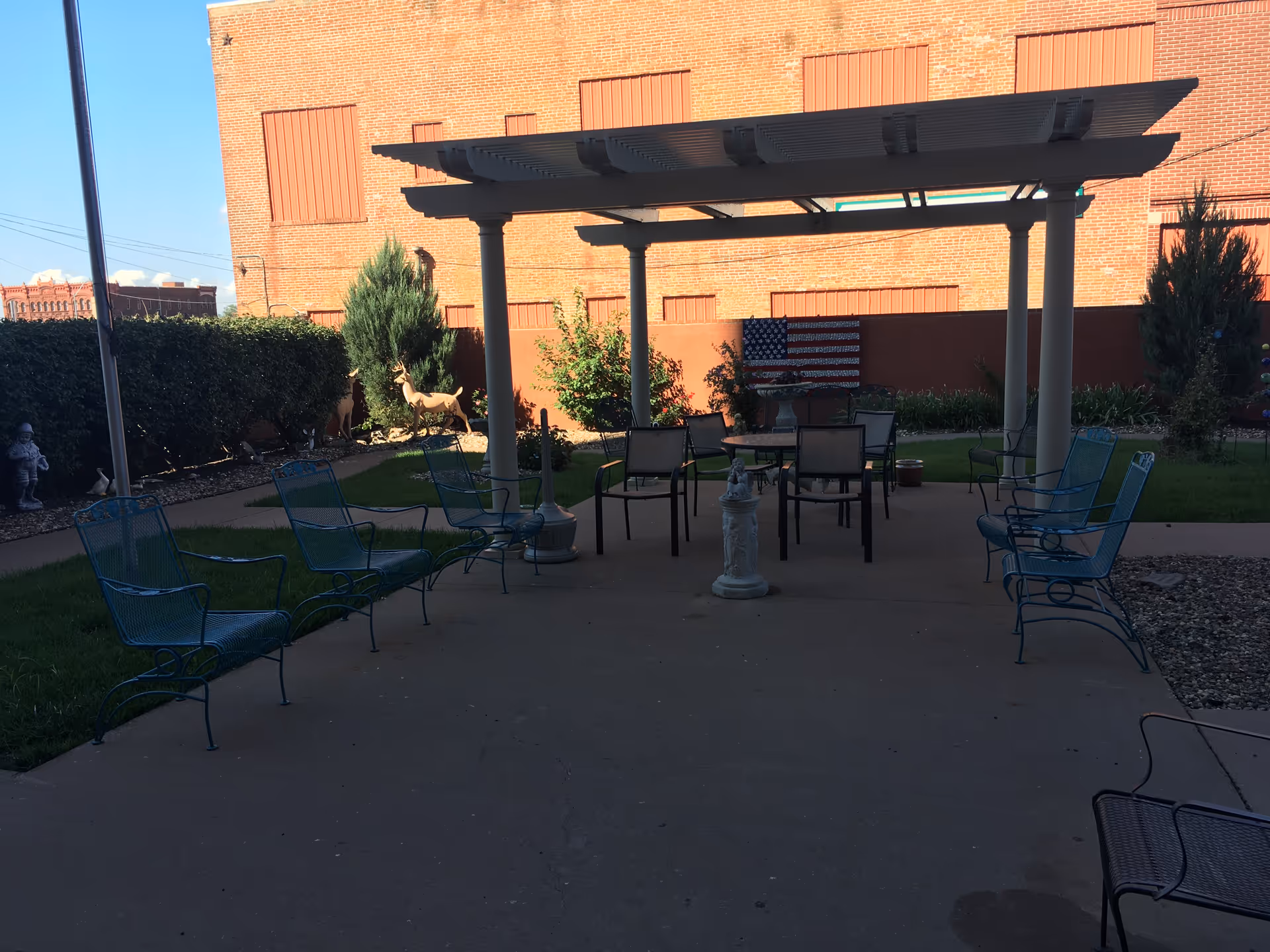 Outdoor courtyard with blue metal chairs around a pergola and central statue.