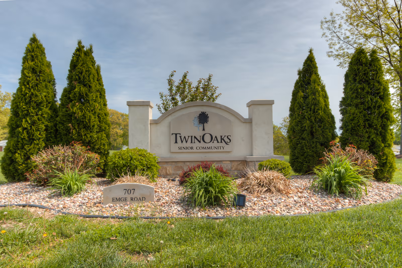 Entrance monument sign for Twin Oaks senior community set in landscaped rocks and evergreens.
