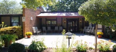 Brick Woodlands of Findlay Assisted Living entrance with outdoor seating and greenery.