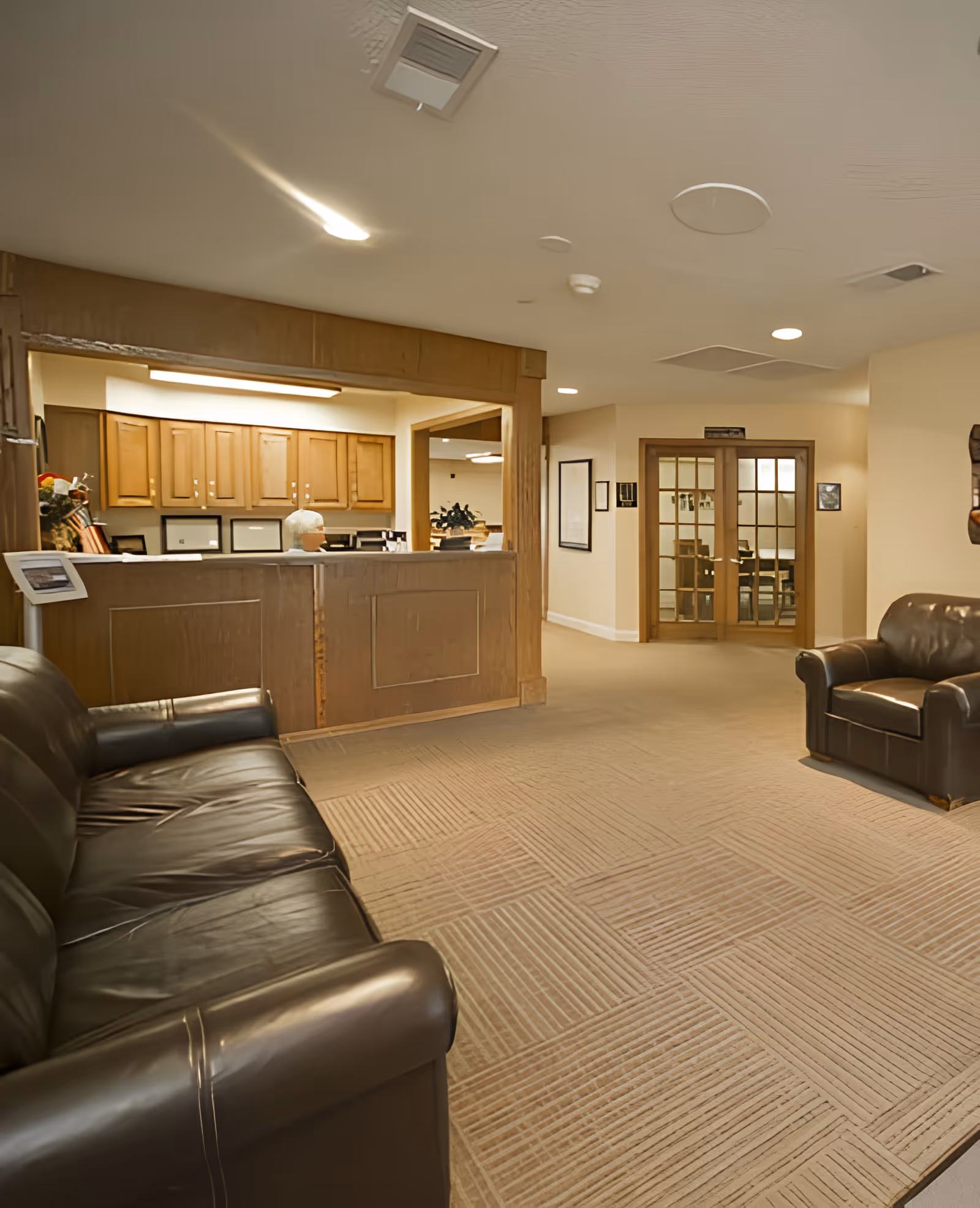 Reception lobby with leather sofas facing a wooden front desk and glass-door office in the background.