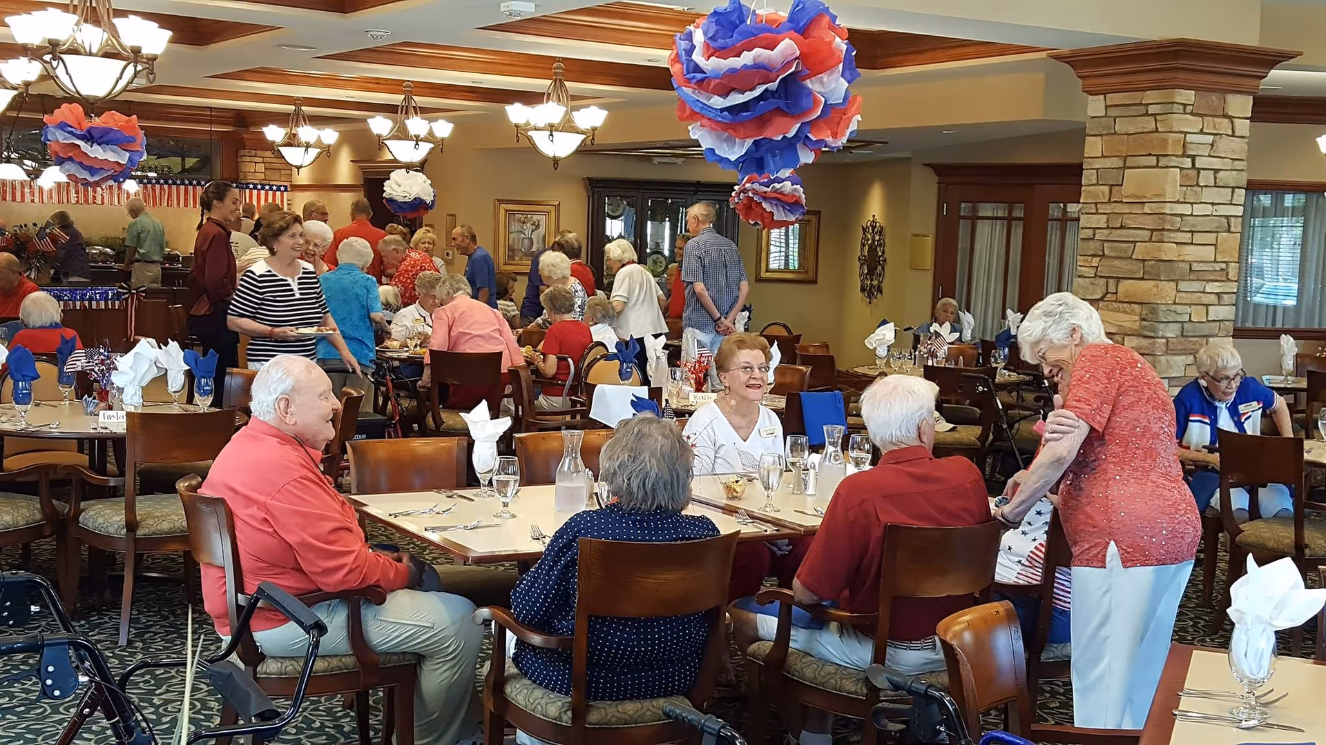 Elderly residents socializing and dining in a decorated communal dining room at a retirement community.