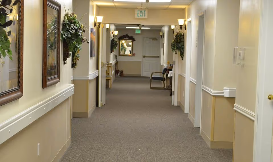 Carpeted interior hallway with handrails, framed artwork, wall sconces and an exit sign at the far end.