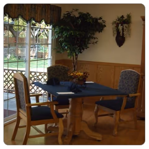 A small dining table with four upholstered chairs next to a sliding glass door, a potted plant, and wall decorations.
