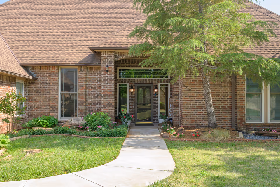 Brick senior living facility with a front entrance, walkway, and landscaped greenery.