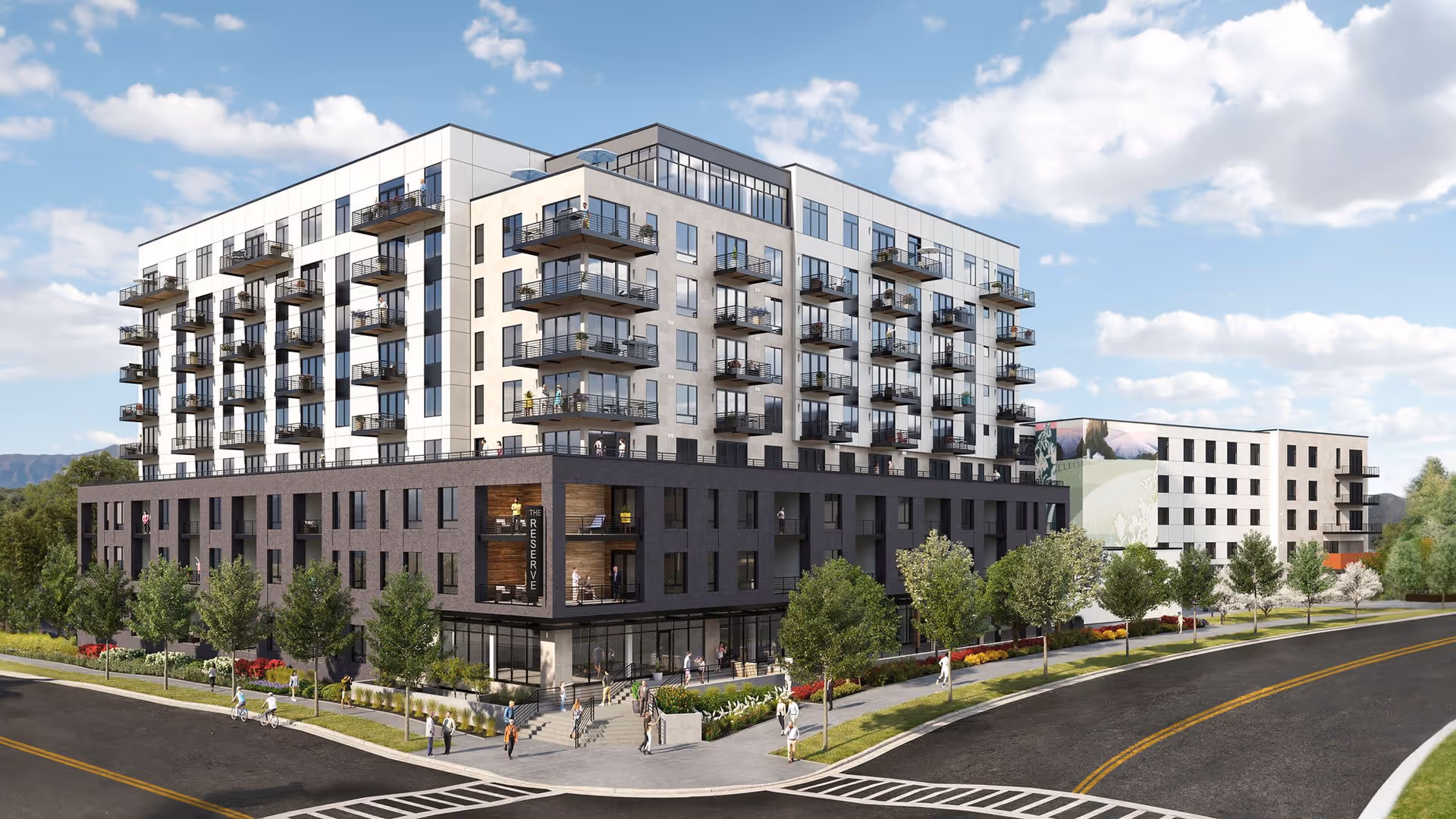 Exterior view of a modern multi-story senior living facility named The Reserve at Lone Tree, featuring balconies, large windows, landscaped sidewalks with trees and bushes, and people walking and biking around the building on a sunny day with blue sky and clouds.