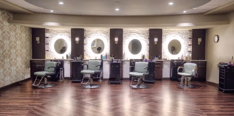 Empty salon area with five styling stations, round mirrors, and vintage barber chairs against a backlit stone wall.