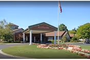 Front entrance of Woodbrook Assisted Living Residence with a covered porte-cochere, an American flag, and a landscaped circular driveway.