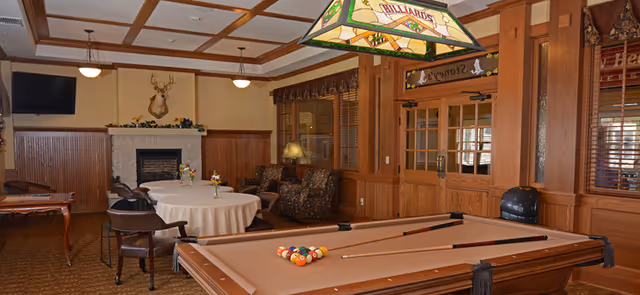 Cozy wood-paneled common room with a pool table, round table with chairs, fireplace, TV, and lounge seating.