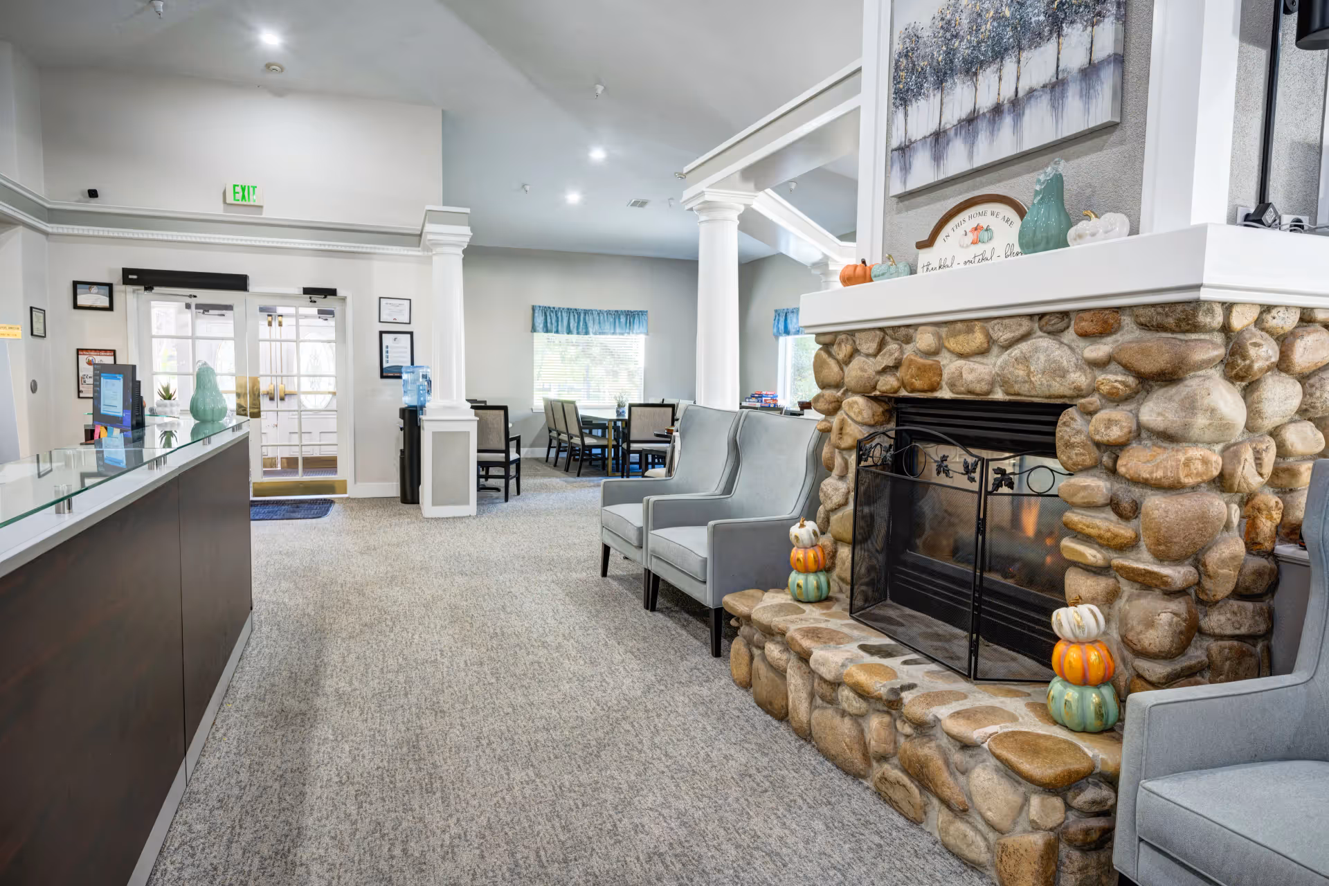 Lobby reception and seating area featuring a stone fireplace, upholstered chairs, a glass-topped desk, and the front entrance.