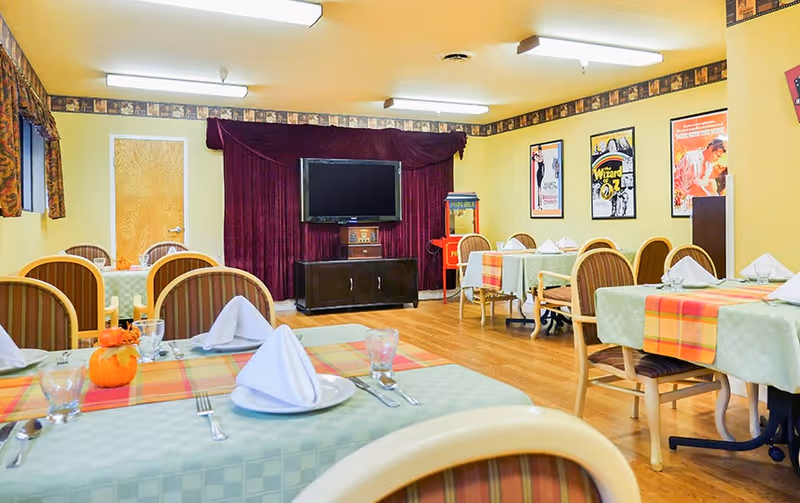 Dining room with several neatly set tables, a TV on a cabinet against a curtain backdrop, and movie posters on the wall.