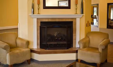 Two beige armchairs flank a fireplace in Regency Care Center's cozy living room.