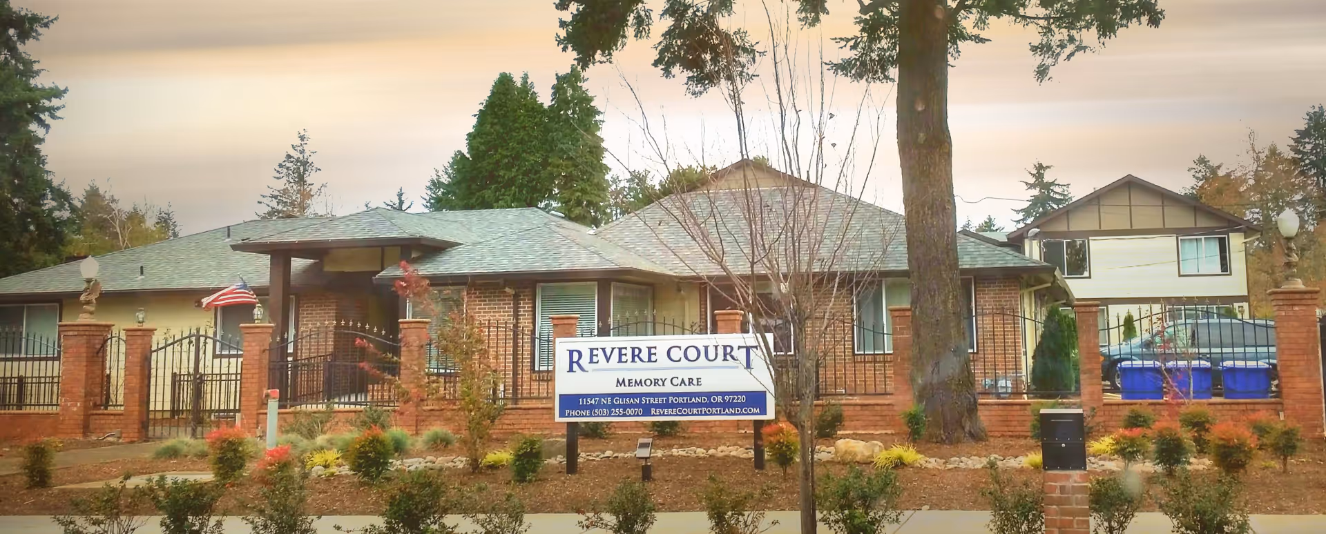 Front exterior of Revere Court Memory Care building with brick facade, gated entrance, landscaping, and a sign in the foreground.