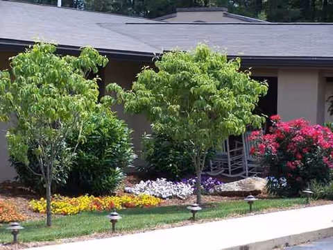 Exterior view of Haywood Lodge with trees, shrubs, and colorful flowers.