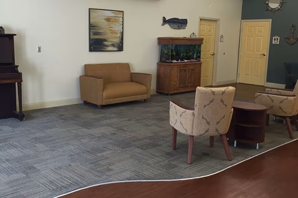 A common-area seating room with upholstered chairs and a loveseat, a fish tank, a piano, and wall decorations.