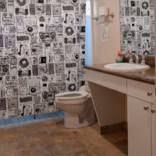 Bathroom featuring a toilet, sink, countertop, and bold patterned wallpaper in a senior living facility.