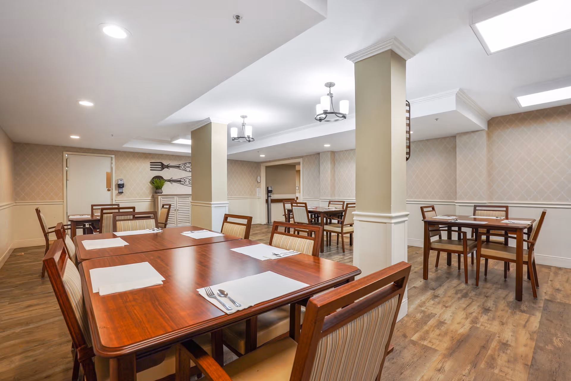Bright dining room with multiple wooden tables and chairs arranged with placemats and utensils.