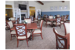 Communal dining room with multiple wooden tables and upholstered chairs, floral centerpieces, and a fireplace with a TV.