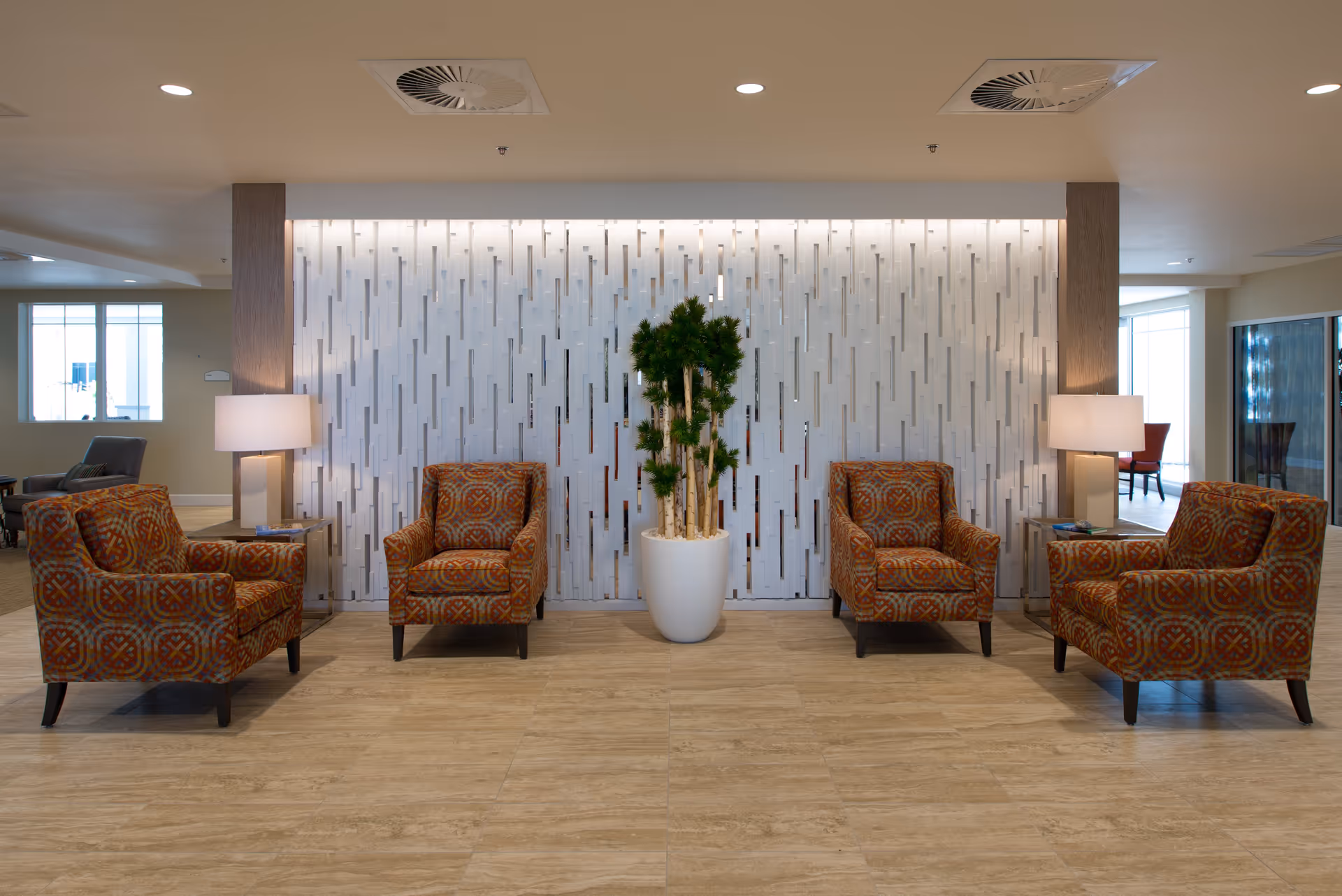 Lobby seating area with four patterned armchairs arranged around a potted plant in front of a decorative partition wall.