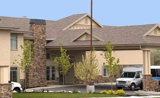 Exterior view of Carrington Court Assisted Living and Memory Care building with a driveway and trees.