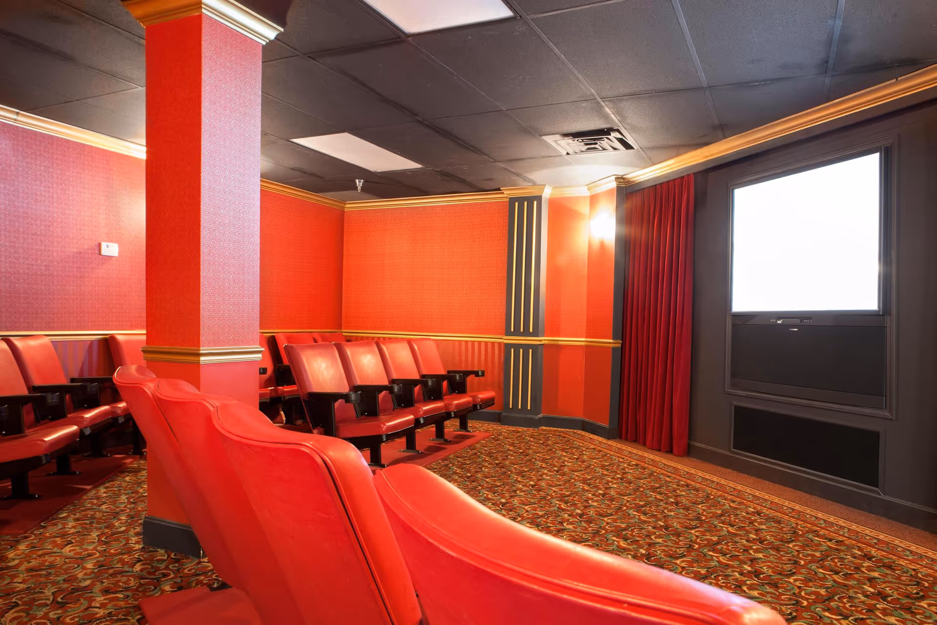 Private screening room with rows of red theater seats, patterned carpet, and a blank screen at the front.