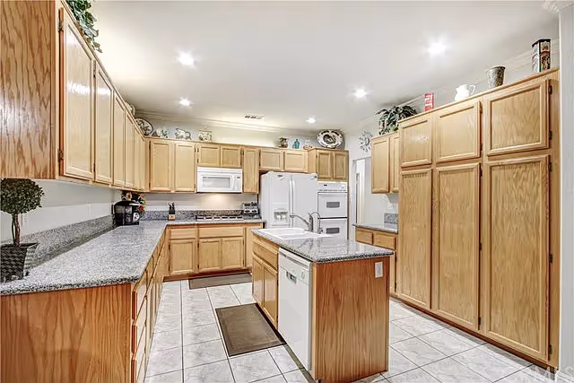 Bright, spacious kitchen with oak cabinets, a center island, white appliances, and tiled flooring.