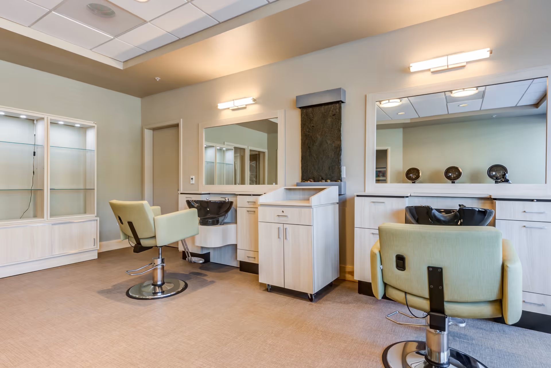 Bright salon interior with two styling chairs, shampoo bowls, large mirrors, and light wood cabinetry.