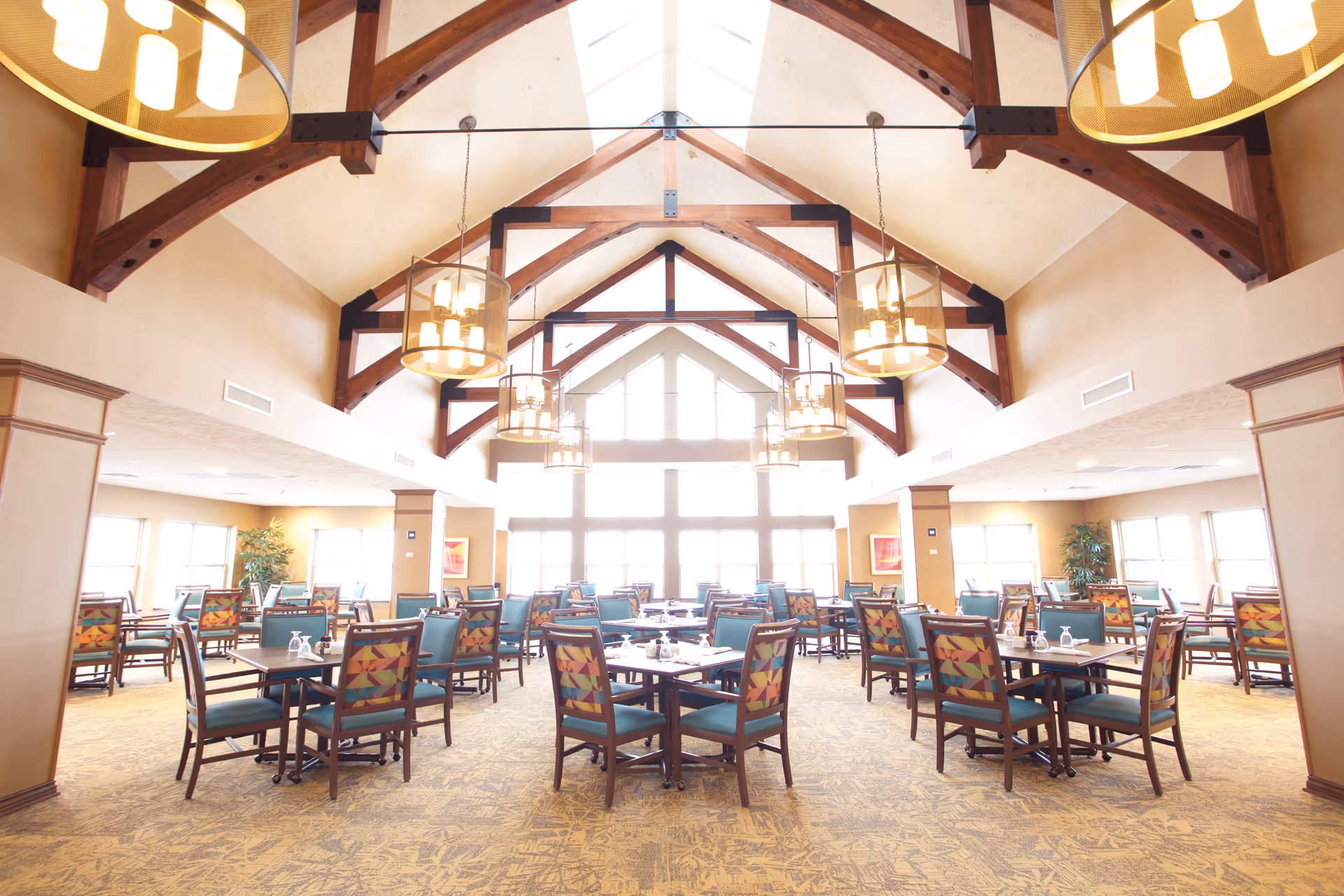 Bright, spacious dining room with vaulted wooden-beam ceiling, hanging pendant lights, and multiple tables and chairs set for dining.
