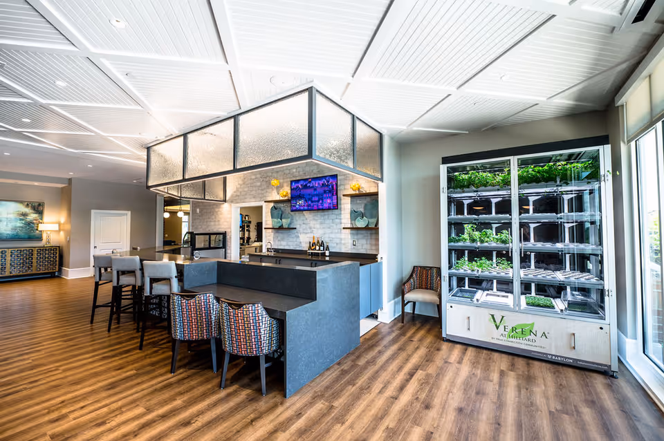 Bright communal kitchen and seating area with a central island, bar stools, and a vertical indoor garden labeled "Verena at Hilliard".