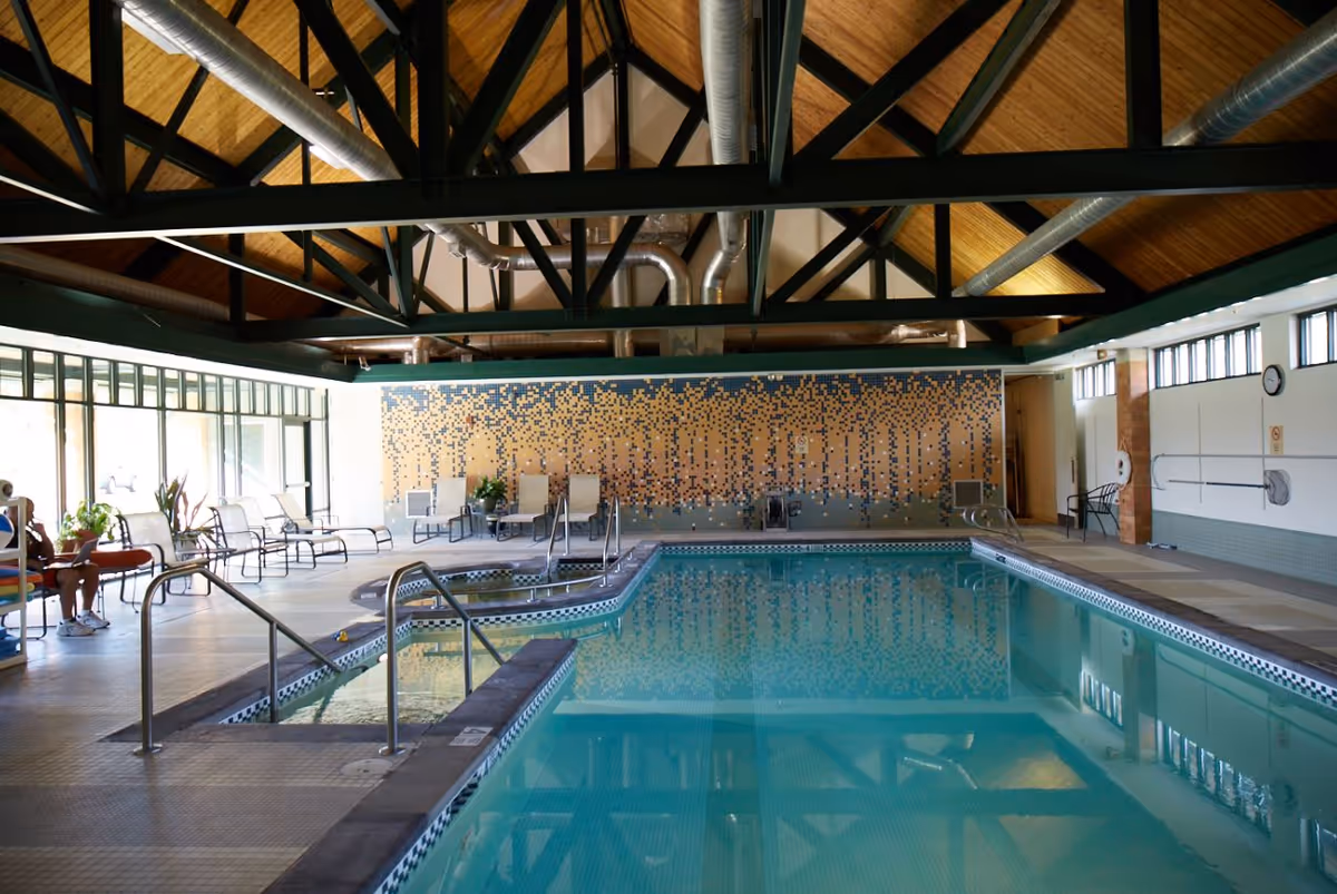 Indoor swimming pool with lounge chairs, tiled deck, and a high exposed-beam wooden ceiling.