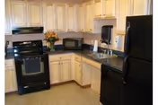 A compact kitchen with light wood cabinets, black appliances, and a vase of flowers on the counter.