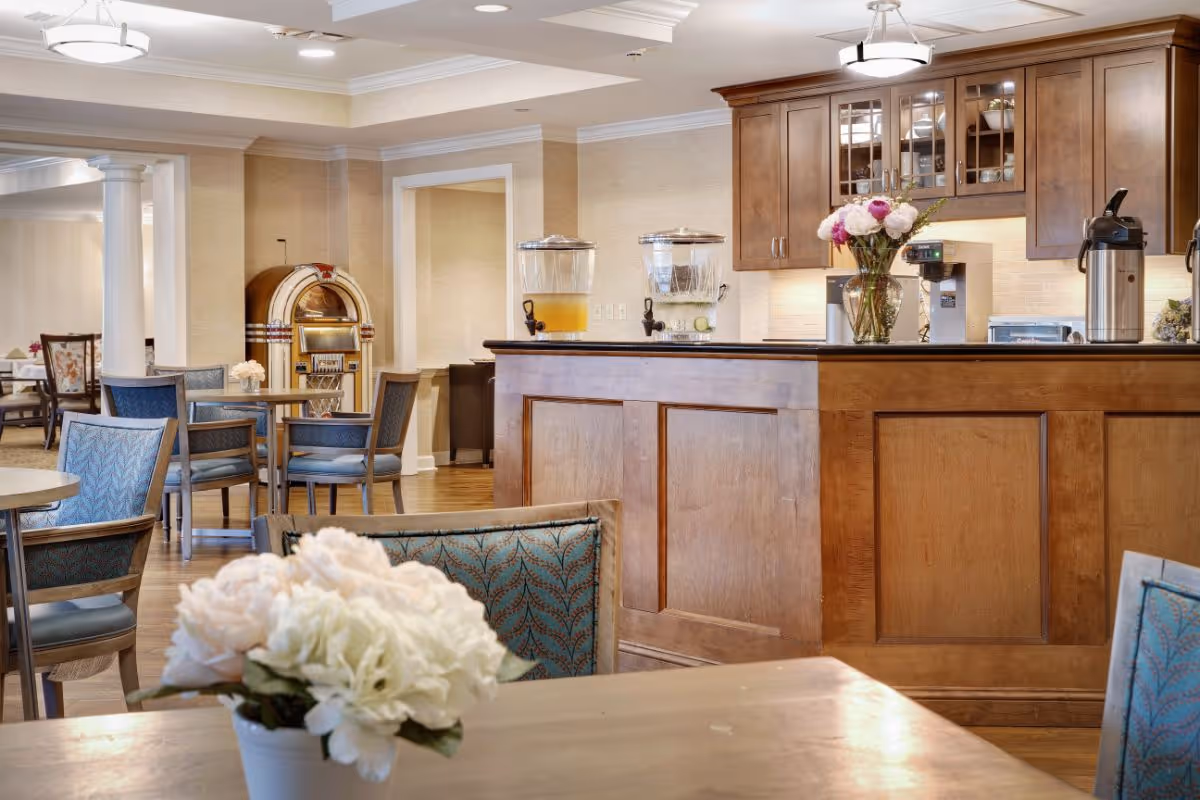 Dining area with a wooden service counter, tables and chairs, floral centerpieces, and a vintage jukebox in the background.