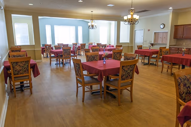 Well-lit dining room with multiple tables covered in red tablecloths and wooden chairs.