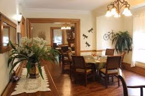Dining room in a senior residence with a table, chairs, plants, and warm lighting.