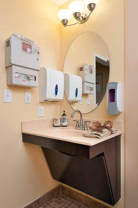 Bathroom sink area with mirror, soap and paper towel dispensers under warm lighting.