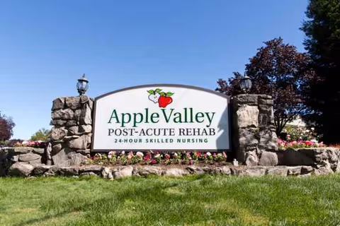 An outdoor stone entrance sign for Apple Valley Post-Acute Rehab with landscaping.