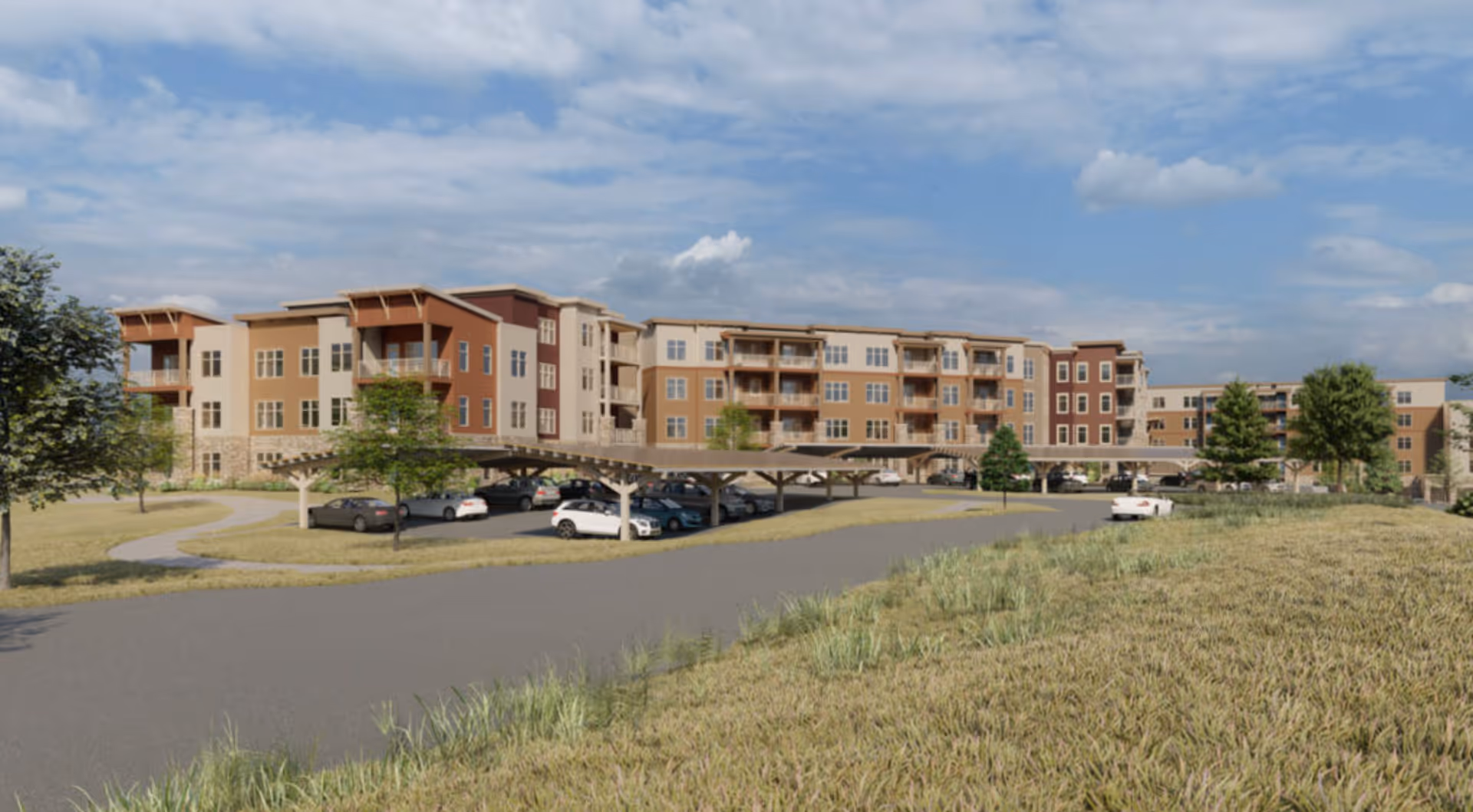 Exterior view of a large, multi-story residential building with balconies, surrounded by a parking area with cars and some trees under a partly cloudy sky.