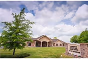 Exterior view of Springdale Health and Rehabilitation Center, LLC building with a manicured lawn, a tree in the foreground, and a sign displaying the facility's name. The sky is partly cloudy.