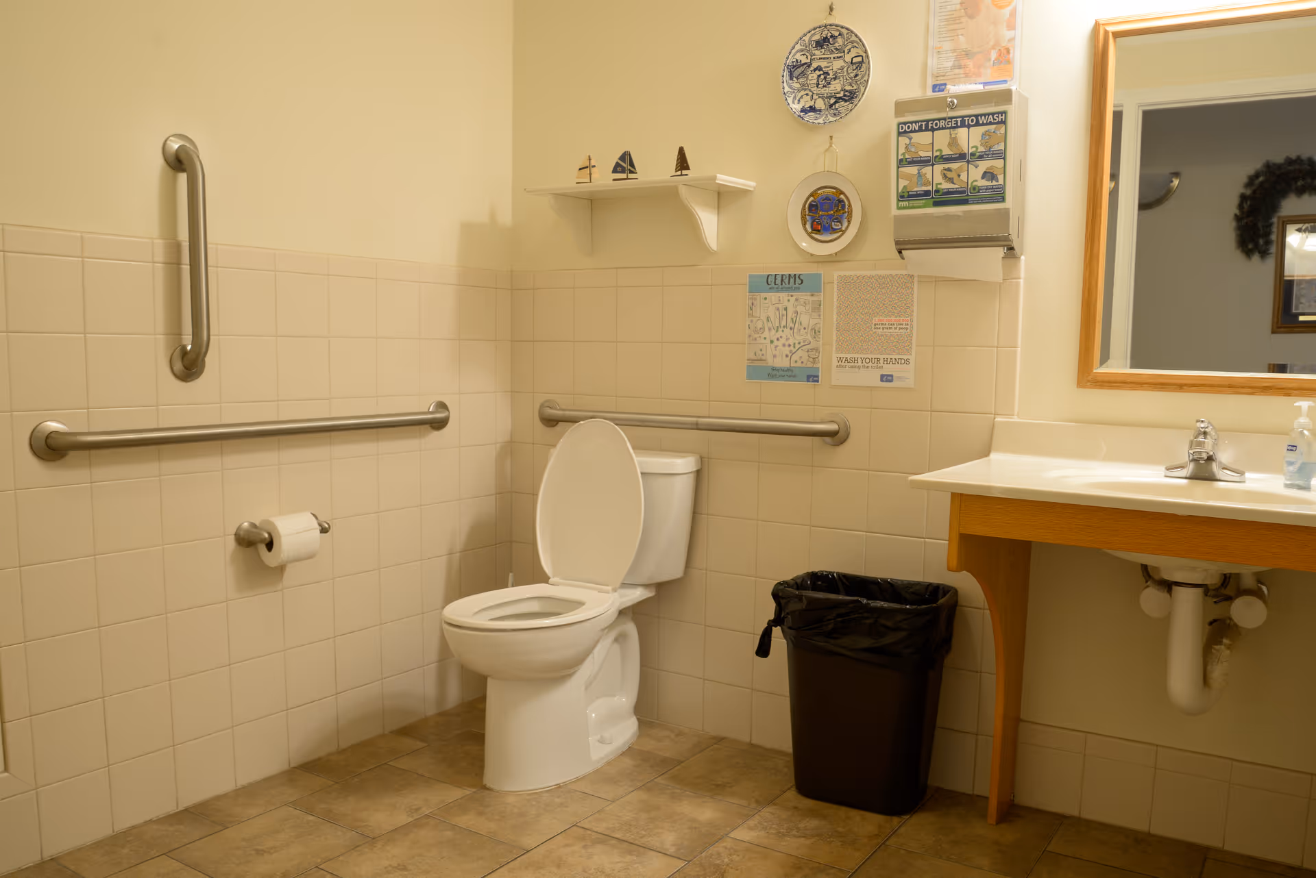 Accessible bathroom with a toilet, grab bars, a sink and mirror, and a trash can.