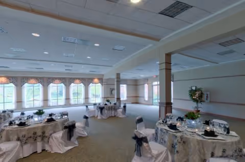 Bright banquet-style dining room with round tables set for an event and large windows along one wall.